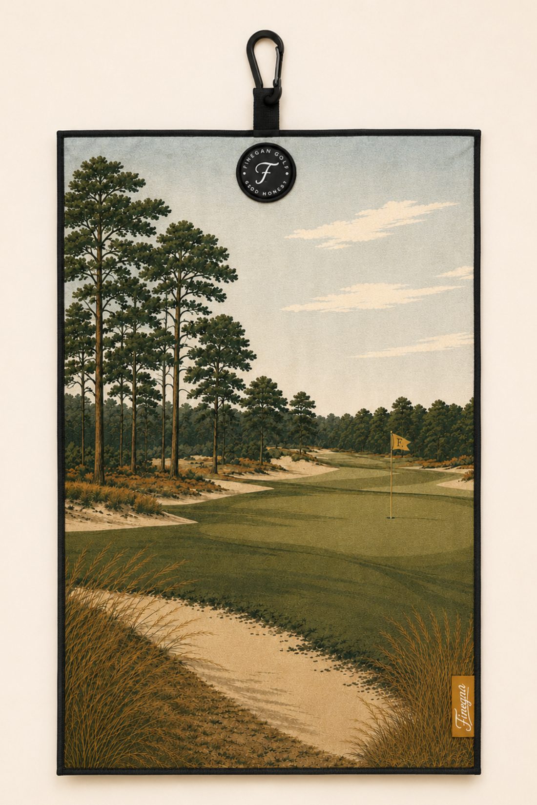The Sandhills towel — a painted pine and sand fairway, printed edge to edge, with carabiner clip and Finegan Golf badge